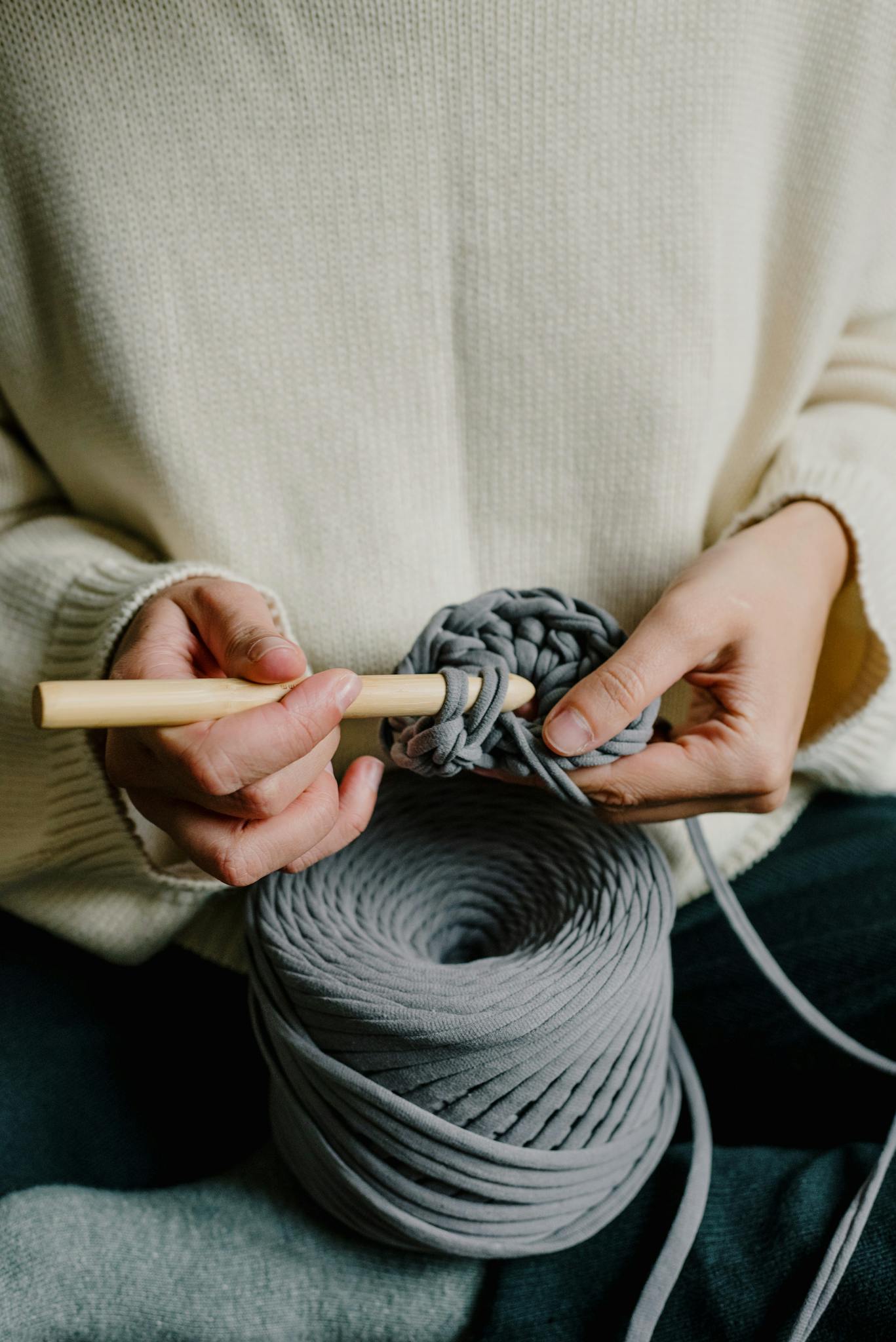 Hands crocheting with gray yarn and a wooden hook, close-up.