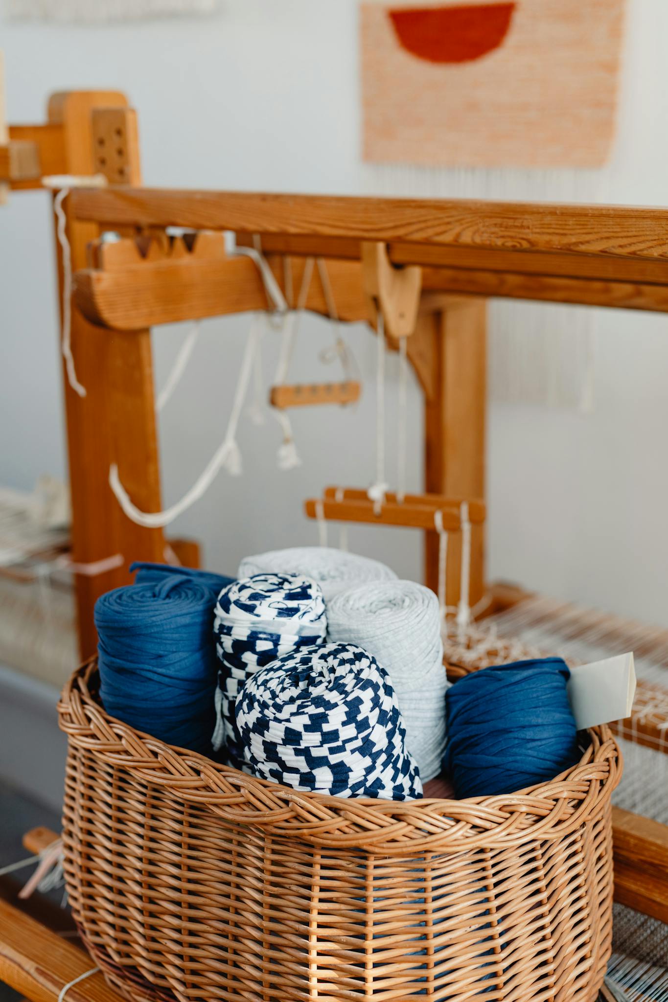 Vertical shot of yarn in a wicker basket beside a wooden loom indoors.